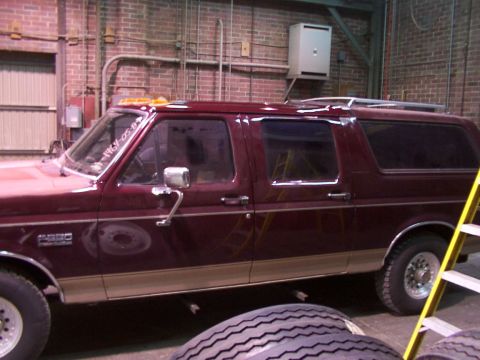 1988 Ford C-350 (Centurion Conversions) - Side view of a maroon Ford Bronco SUV with tan trim, parked indoors near a ladder and tires.