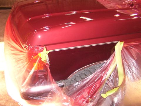 1988 Ford C-350 (Centurion Conversions) - A red truck fender and hood are covered in plastic sheeting and taped off, suggesting preparation for painting.