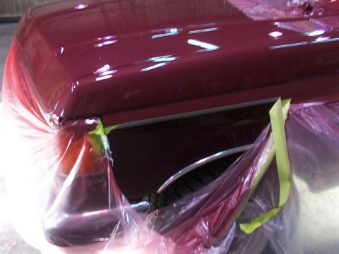 1988 Ford C-350 (Centurion Conversions) - The fender and hood edge of a maroon vehicle are covered in plastic sheeting and tape, suggesting it is undergoing repair or painting.