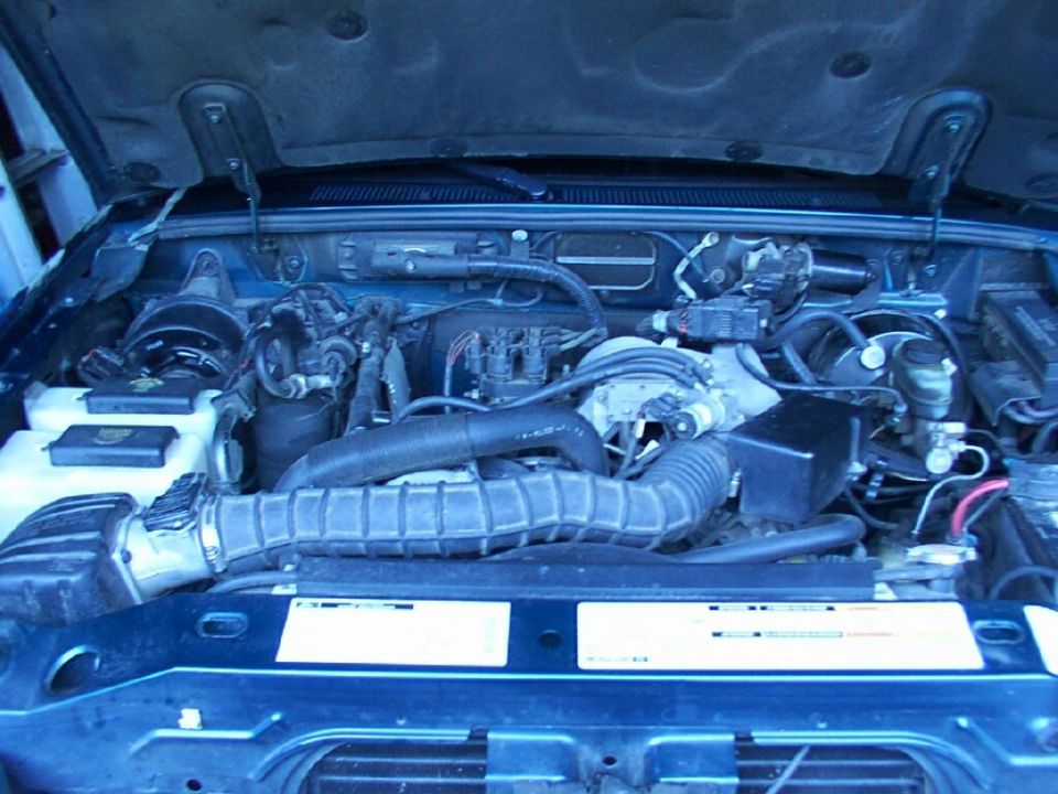 Engine bay of a blue 1998 Ford Ranger with hood open, showing air intake hose and reservoirs
