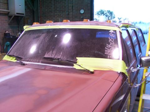 1988 Ford C-350 (Centurion Conversions) - A red Ford truck's windshield is taped off, ready for paint. Writing on the glass indicates a date or identifier.