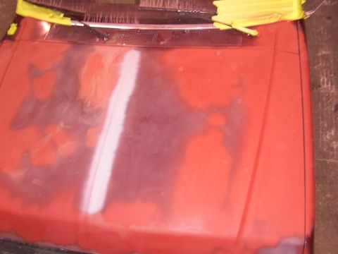 1988 Ford C-350 (Centurion Conversions) - Close-up of a red car hood undergoing bodywork, showing primer and masking tape.