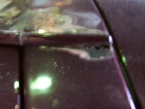 1988 Ford C-350 (Centurion Conversions) - Close-up of damaged dark red vehicle body panel showing rust and primer.