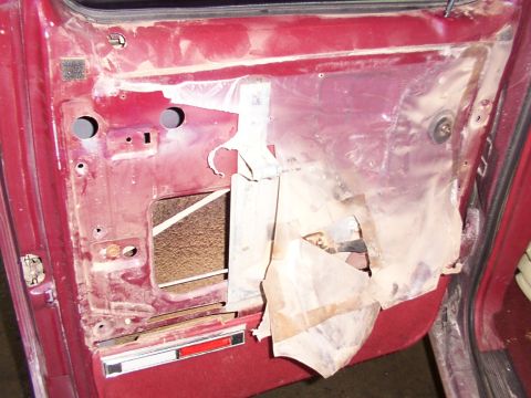 1988 Ford C-350 (Centurion Conversions) - The interior of a car door shows exposed metal and a torn plastic vapor barrier, indicating disassembly.
