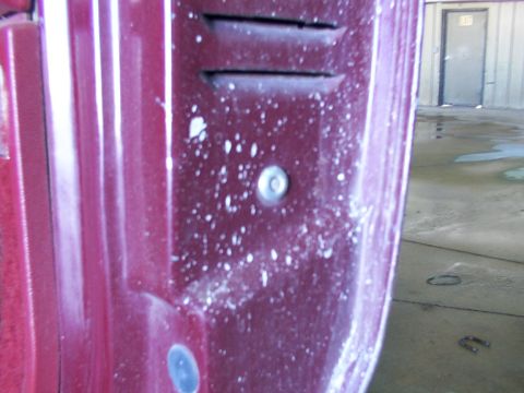 1988 Ford C-350 (Centurion Conversions) - Detail of a red vehicle panel with vents and a fastener, possibly a door lock motor housing.