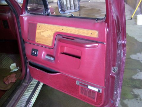 1988 Ford C-350 (Centurion Conversions) - The interior door panel of a vehicle shows red upholstery, wood grain accents, and a speaker grille.