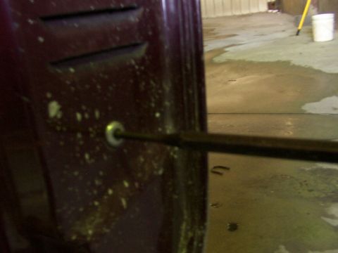 1988 Ford C-350 (Centurion Conversions) - A screwdriver is inserted into a hole on a vehicle's door panel, likely for maintenance on the lock mechanism.
