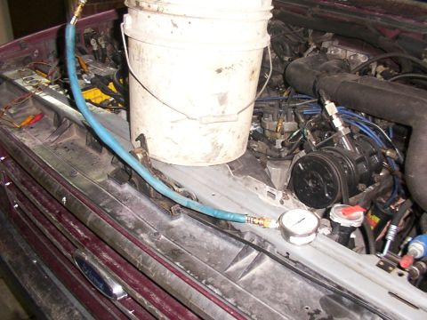 1988 Ford C-350 (Centurion Conversions) - A fuel pressure test is being conducted on the engine of a vehicle, with a bucket and gauge visible.
