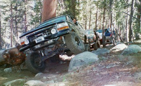 1994 Ford Bronco - Multiple off-road vehicles traverse a forest trail with large boulders.
