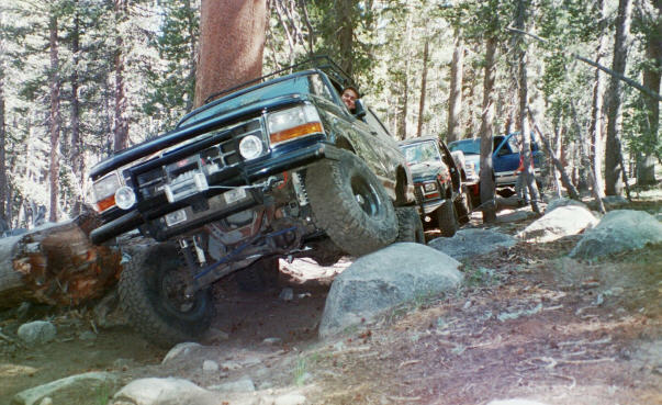 Dark green Ford SUV flexing suspension over boulders on a wooded off-road trail