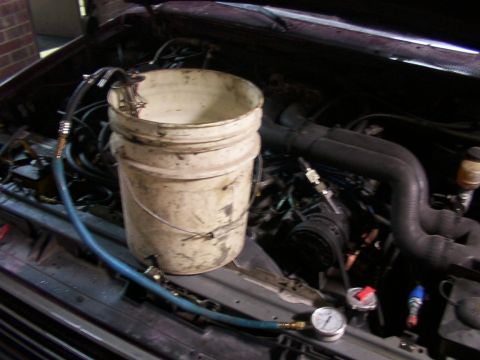 1988 Ford C-350 (Centurion Conversions) - A bucket is used to test fuel pressure in the engine bay, with hoses and a gauge visible.