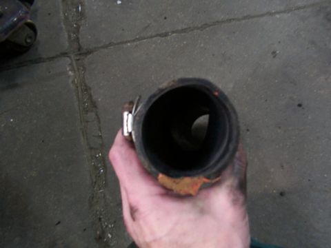 1988 Ford C-350 (Centurion Conversions) - A hand holds a rubber hose with a metal clamp, revealing orange corrosion at its opening.