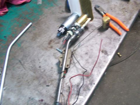 1988 Ford C-350 (Centurion Conversions) - A disassembled fuel pump assembly, including a metal tube and wiring, rests on a workbench next to a pair of pliers.