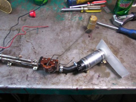 1988 Ford C-350 (Centurion Conversions) - Fuel pump assembly with sender unit and filter sock on a workbench, surrounded by tools.