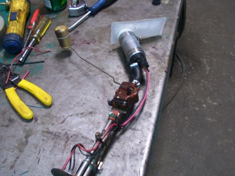 1988 Ford C-350 (Centurion Conversions) - A fuel pump assembly, complete with a float and wiring, lies on a workbench next to various tools.