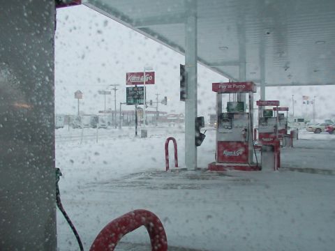 1988 Ford C-350 (Centurion Conversions) - Gas pumps are visible at a Kum & Go station during a heavy snowfall, with prices displayed on a sign.