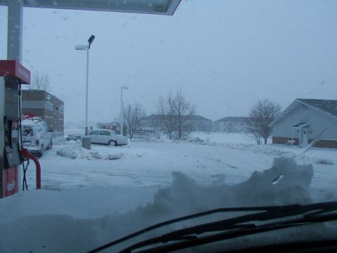 1988 Ford C-350 (Centurion Conversions) - A snowy scene at a gas station with multiple vehicles partially buried in snow.