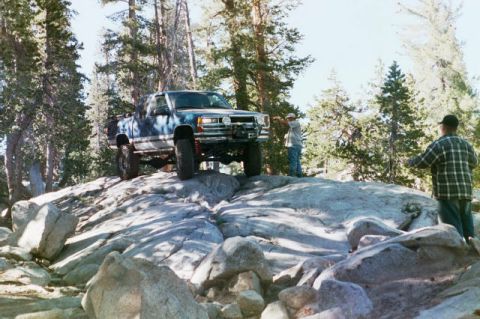 1994 Ford Bronco - A blue pickup truck navigates a rocky trail in a wooded area.