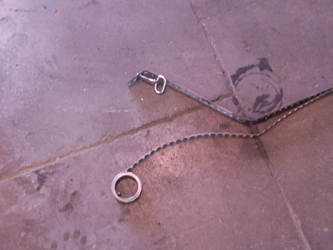 1988 Ford C-350 (Centurion Conversions) - A detached fuel tank strap lies on the ground, showing its metal construction and attachment points.