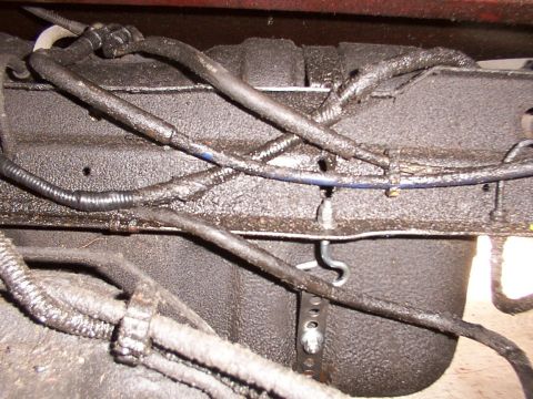 1988 Ford C-350 (Centurion Conversions) - Underside view of a vehicle's fuel tank straps and associated wiring, showing wear and grime.