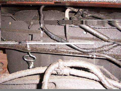 1988 Ford C-350 (Centurion Conversions) - Close-up of the undercarriage shows fuel tank straps and electrical wiring, with a metal bracket attached.