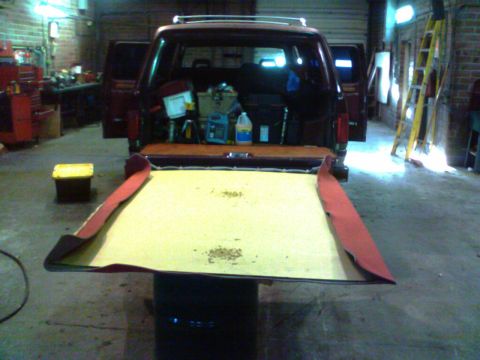 1988 Ford C-350 (Centurion Conversions) - The interior of a van or SUV is visible with the tailgate open, revealing stored items and a yellow toolbox nearby.