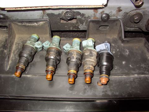 1988 Ford C-350 (Centurion Conversions) - A set of five fuel injectors, showing varying degrees of wear and tear, are laid out for inspection.