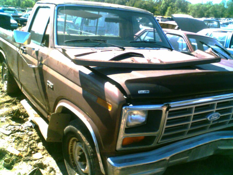 Brown Ford pickup truck, front view, in a junkyard