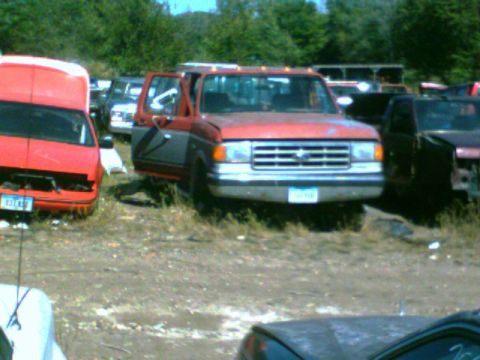 1988 Ford C-350 (Centurion Conversions) - This red and gray pickup truck, likely from the 1980s, is parked in a junkyard with its driver's door ajar.