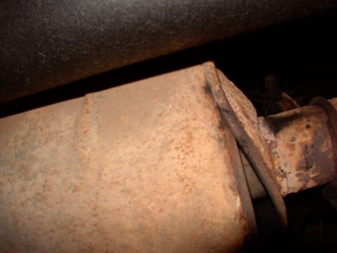 1988 Ford C-350 (Centurion Conversions) - Close-up of a rusty muffler and exhaust pipe, showing signs of wear and tear.