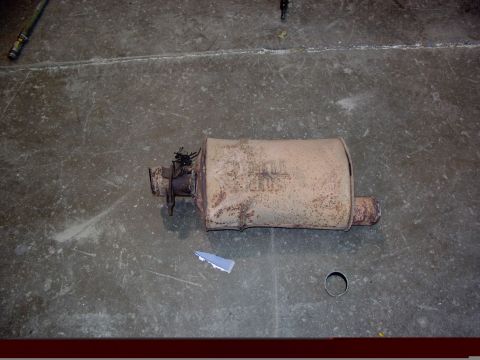 1988 Ford C-350 (Centurion Conversions) - A rusty muffler lies on a concrete floor, showing some visible text on its surface.