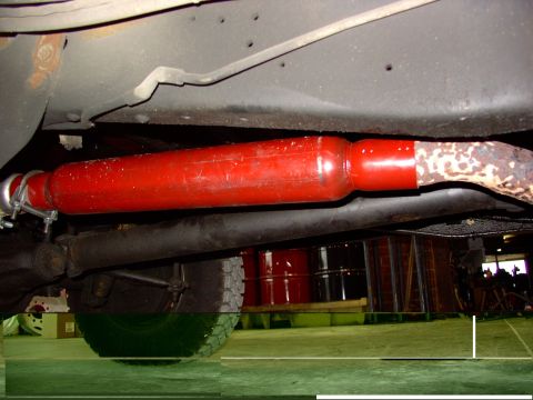 1988 Ford C-350 (Centurion Conversions) - Close-up view of a red-painted exhaust component connected to a rusted pipe under a vehicle.