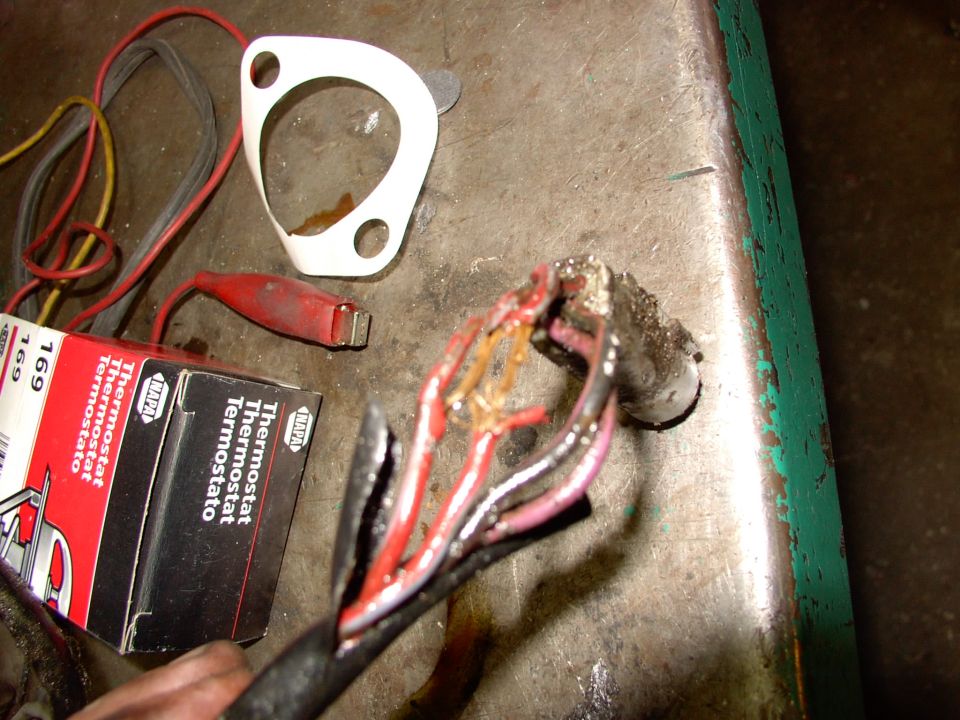 Burned wiring pigtail with melted red and pink wires beside NAPA 169 thermostat box and gasket