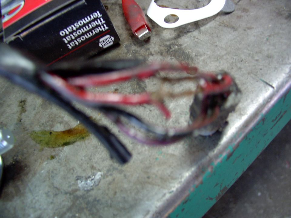 Burnt melted wiring connector with charred red wires beside NAPA thermostat box on workbench