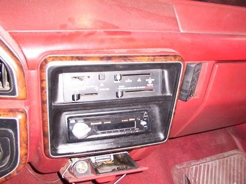 1988 Ford C-350 (Centurion Conversions) - Close-up of the dashboard showing an aftermarket stereo installed below the climate controls in a vehicle with a red interior and wood grai…