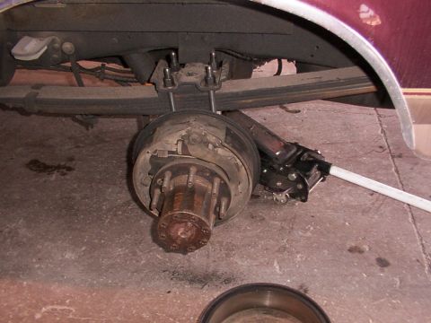 1988 Ford C-350 (Centurion Conversions) - The rear brake assembly of a vehicle is shown, with the drum removed and a jack positioned to support the axle.