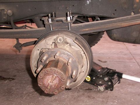 1988 Ford C-350 (Centurion Conversions) - Close-up of a rear drum brake assembly on a vehicle, with a hydraulic jack visible.