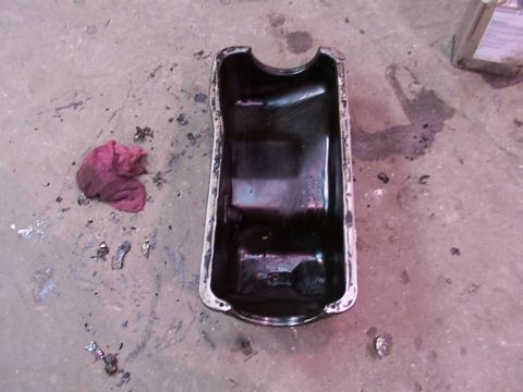 1988 Ford C-350 (Centurion Conversions) - A removed oil pan sits on the floor next to a stained rag and scattered metal fragments.
