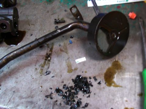 1988 Ford C-350 (Centurion Conversions) - Oil pickup tube and screen removed from an engine, with metal debris scattered on the workbench.