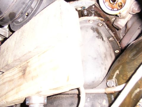 1988 Ford C-350 (Centurion Conversions) - Close-up view of an engine's oil pan, showing signs of a leak and a wooden block used for support.