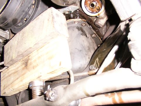 1988 Ford C-350 (Centurion Conversions) - Close-up view of an engine's oil pan, temporarily supported by a wooden block during maintenance.