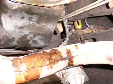 1988 Ford C-350 (Centurion Conversions) - The underside of a vehicle reveals a leaking exhaust pipe and associated mechanical parts.