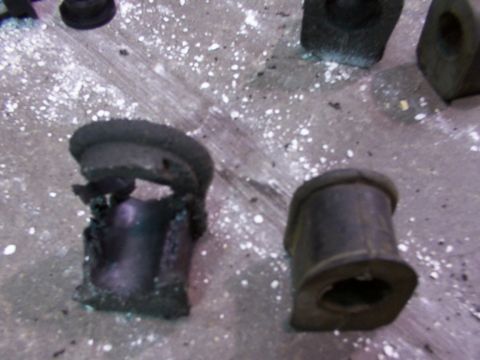 1988 Ford C-350 (Centurion Conversions) - Two rubber suspension bushings, one severely degraded, lie on a concrete surface.