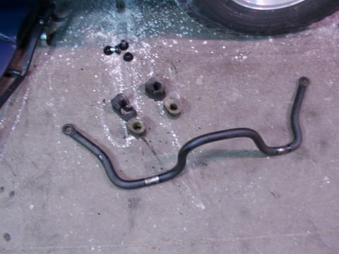 1988 Ford C-350 (Centurion Conversions) - A removed sway bar and its associated bushings and nuts lie on a concrete surface, suggesting a repair or replacement.