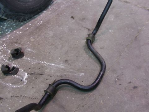 1988 Ford C-350 (Centurion Conversions) - A detached sway bar and its mounting bushings lie on a concrete surface, possibly awaiting installation or replacement.