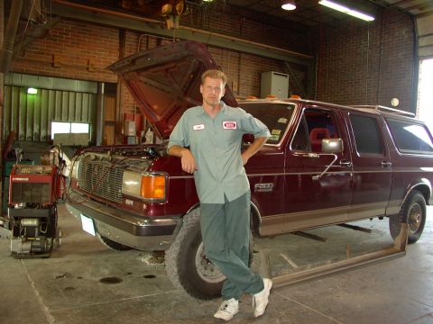 1988 Ford C-350 (Centurion Conversions) - Mechanic stands next to a maroon Ford Bronco SUV in a garage with the hood up.