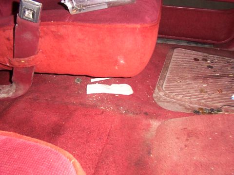 1988 Ford C-350 (Centurion Conversions) - The floor of a vehicle's interior shows red carpet, a seatbelt, and debris including some debris.