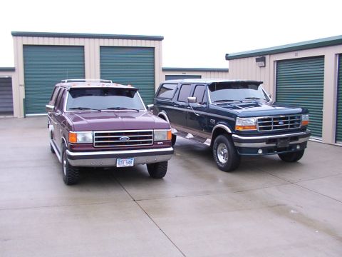 1988 Ford C-350 (Centurion Conversions) - Two Ford SUVs, one purple and one dark blue, are parked outside storage units. The purple SUV has license plate OTV 549.