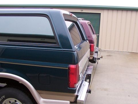 1988 Ford C-350 (Centurion Conversions) - Two SUVs are parked in front of storage units, one dark green and the other burgundy.