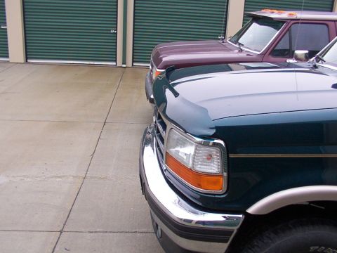 1988 Ford C-350 (Centurion Conversions) - Two trucks are parked side-by-side in front of a row of storage unit doors.
